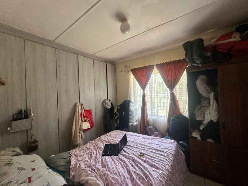 A bedroom featuring built-in cupboards and security burglar bars on the window, showing signs of ceiling wear and maintenance requirements.