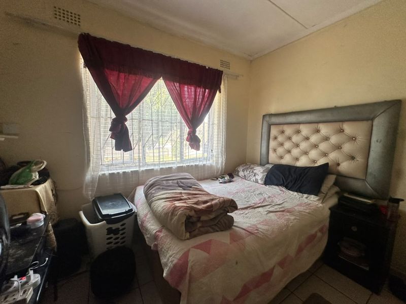 A bedroom featuring tiled flooring, security bars on the window, and a ceiling vent, requiring cosmetic updates to improve its overall condition.