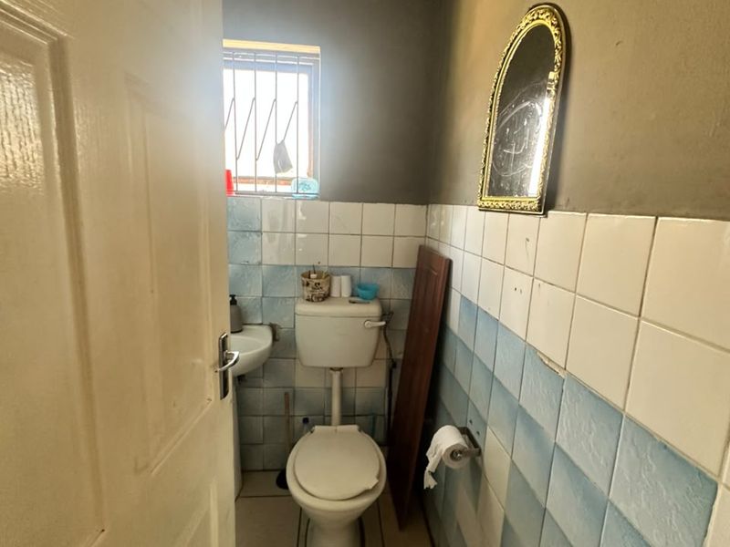 A small bathroom featuring a pedestal basin and toilet, with dated wall tiling and visible signs of wear on the ceiling and walls.