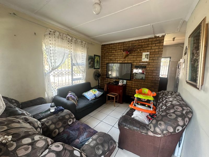 A living room featuring an exposed brick accent wall, ceramic tiled flooring, and security gate access, requiring cosmetic updates to improve its overall condition.