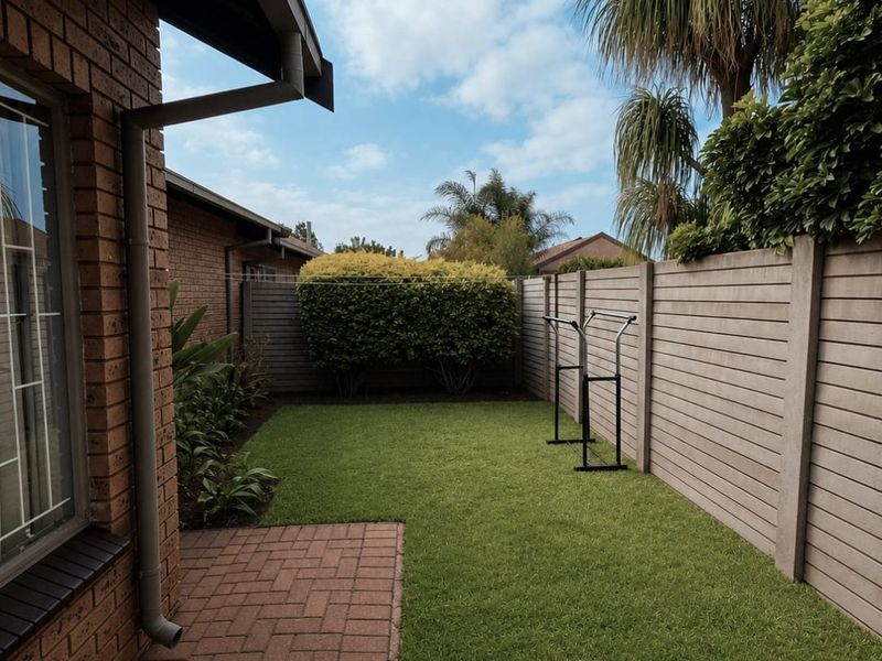A well-maintained rear garden featuring a brick-paved patio, artificial lawn, and secure precast concrete boundary walling.