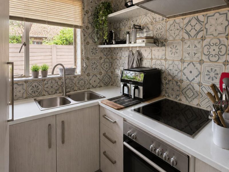 Compact, well-maintained kitchen featuring patterned wall tiles, light wood-finish cabinetry, built-in oven with electric hob, and a double bowl sink.