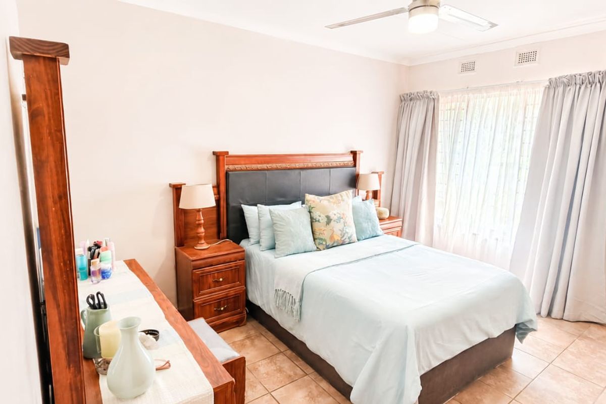 A well-maintained bedroom featuring tiled flooring, a ceiling fan, and a wall-mounted air conditioning unit, offering a comfortable and functional living space.