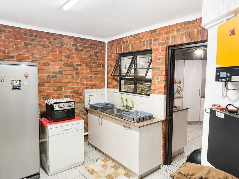 Functional scullery area featuring exposed brick walls, tiled flooring, a double sink, and a wall-mounted solar inverter and battery system.