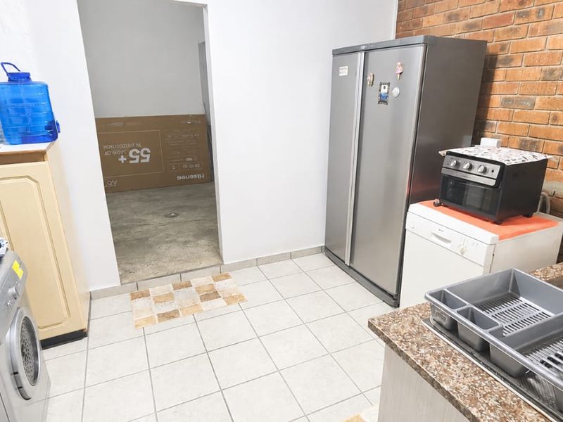 Functional scullery area featuring tiled flooring, exposed brick wall detail, and a double bowl sink with built-in cabinetry.