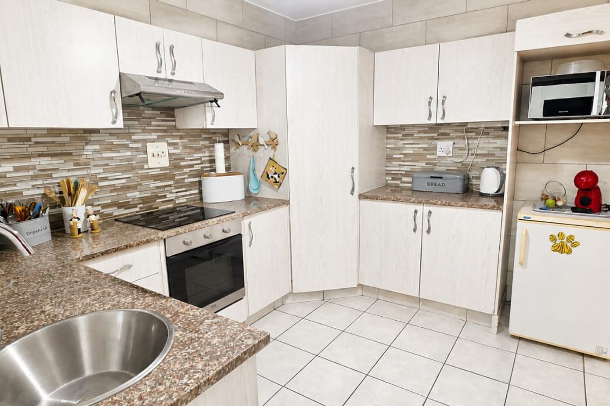 A functional kitchen featuring light wood-grain cabinetry, granite-look laminate countertops, a tiled backsplash, and integrated appliances including an oven and hob.