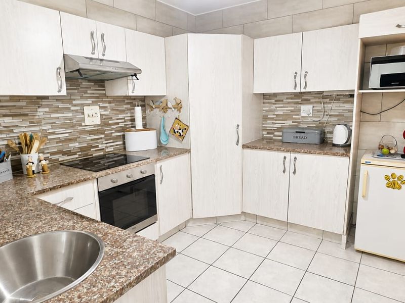 A functional kitchen featuring light wood-grain cabinetry, granite-look laminate countertops, a tiled backsplash, and integrated appliances including an oven and hob.