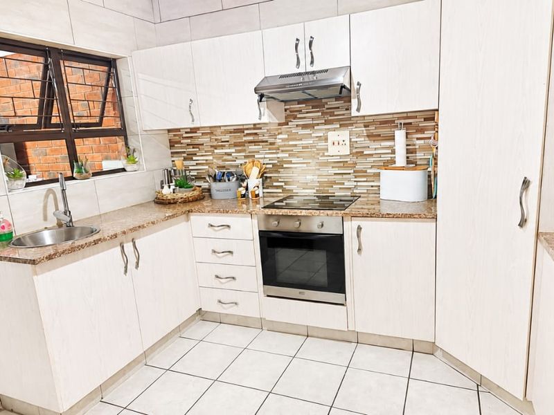 A functional kitchen featuring light-toned cabinetry, granite-look countertops, a built-in oven and hob, and a tiled backsplash with neutral floor tiles.