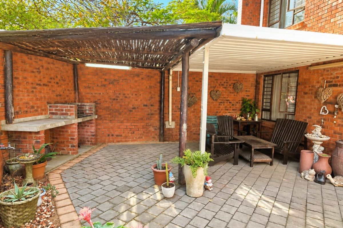 Covered outdoor patio area featuring a built-in brick braai, paved flooring, and a combination of timber and metal roofing structures.