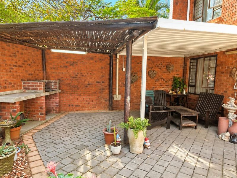 Covered outdoor patio area featuring a built-in brick braai, paved flooring, and a combination of timber and metal roofing structures.