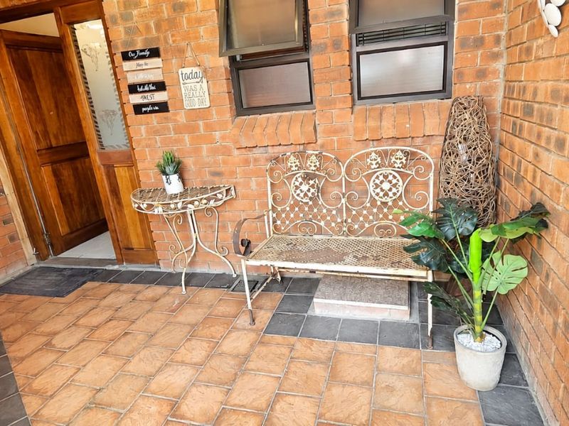 A covered patio area featuring exposed brick walls, tiled flooring, and a timber entrance door, providing a functional outdoor transition space.