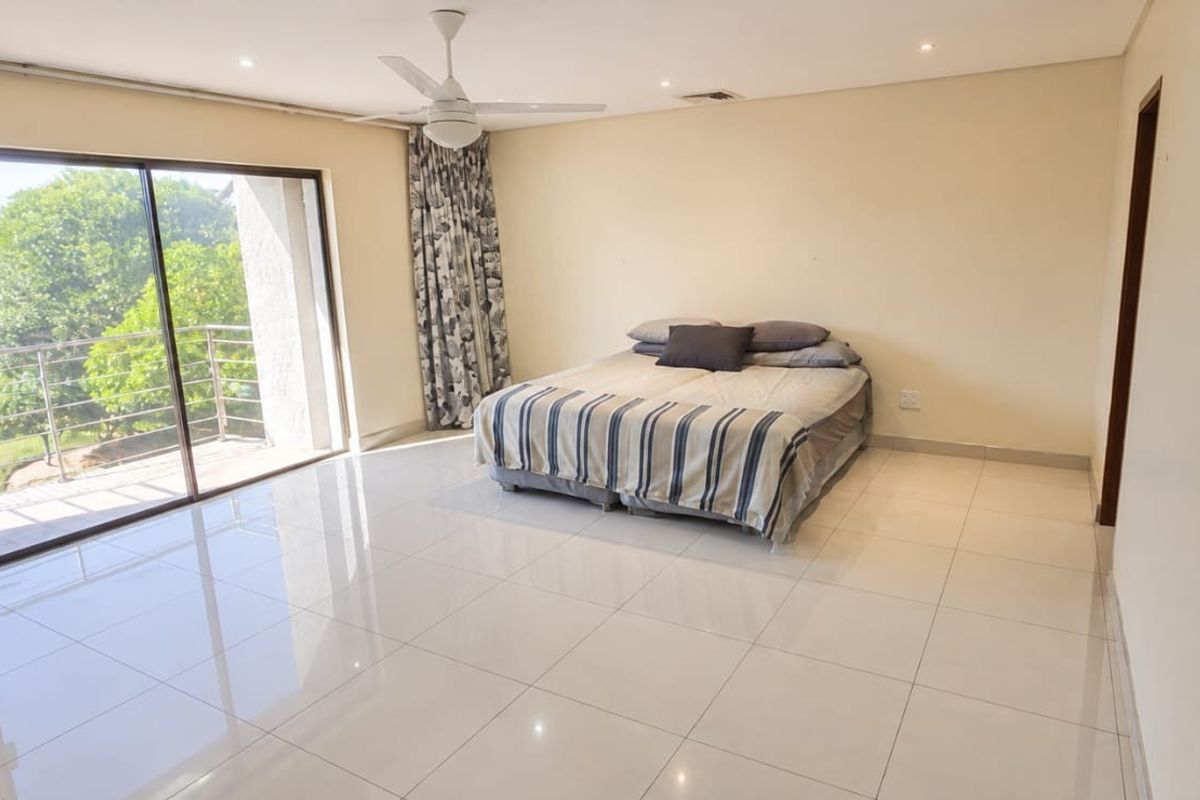 Spacious bedroom featuring polished tile flooring, recessed lighting, a ceiling fan, and large sliding glass doors providing direct access to a private balcony.