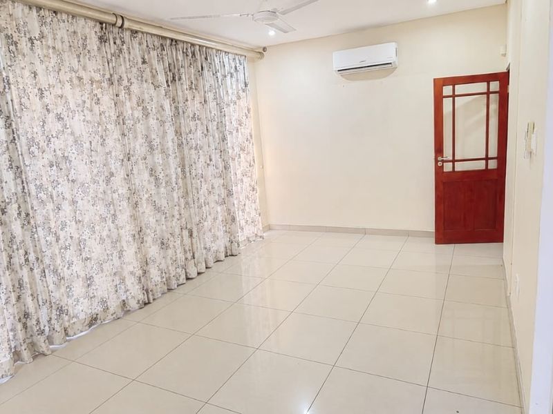 A spacious, empty living area featuring neutral tiled flooring, a split-system air conditioner, ceiling fan, and access to an outdoor space via sliding glass doors.