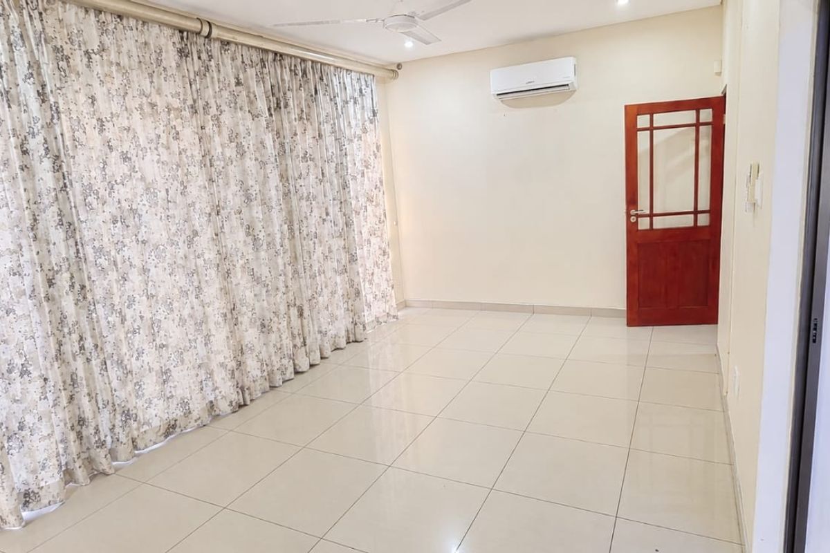 A spacious, empty living area featuring neutral tiled flooring, a split-system air conditioner, ceiling fan, and access to an outdoor space via sliding glass doors.