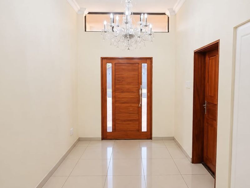 A bright and welcoming entrance hall featuring polished porcelain floor tiles, a solid timber front door, and a classic crystal chandelier.