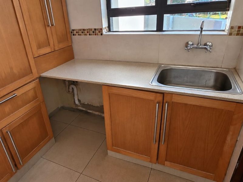 A functional scullery area featuring wooden cabinetry, a stainless steel sink, and stone countertops, with some unfinished wall sections requiring attention.