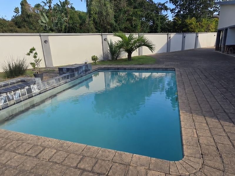 A well-maintained swimming pool area featuring a paved deck, stone-clad water feature, and secure perimeter walling.
