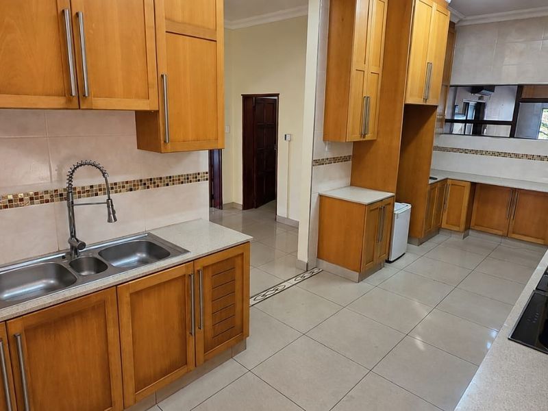 A spacious kitchen featuring wooden cabinetry, stone countertops, a double basin sink, and built-in cooking appliances with neutral tiled flooring.