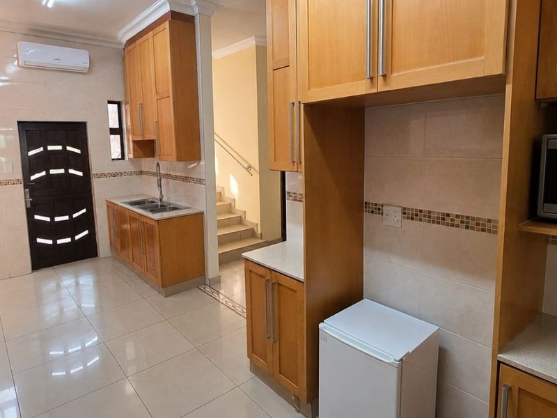 A functional kitchen featuring wooden cabinetry, tiled flooring, a built-in microwave, and a tiled backsplash, with an adjacent staircase leading to another level.