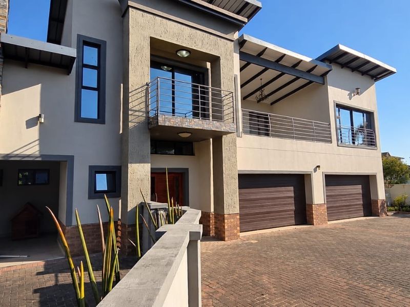 Modern double-story residence featuring stone cladding, a spacious paved driveway, double garage, and upper-level balconies with metal railings.