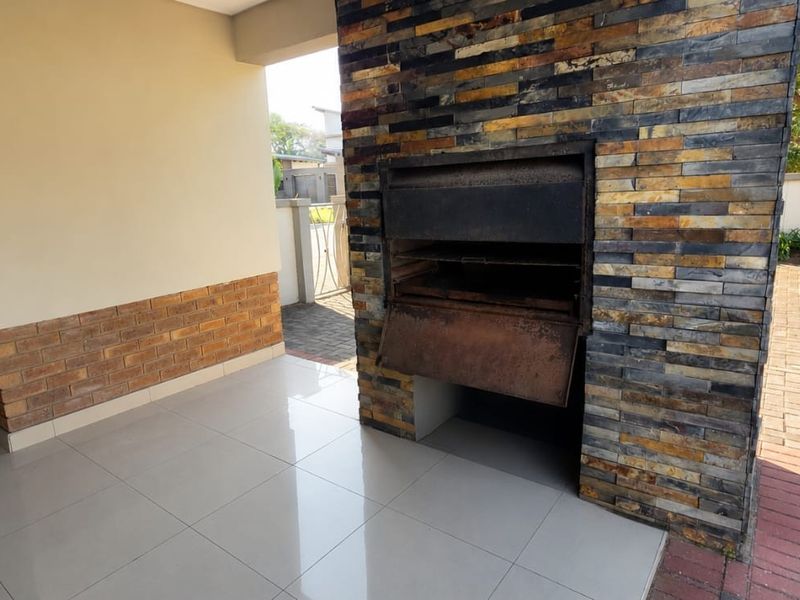 Covered patio area featuring a built-in braai with stone cladding, tiled flooring, and direct access to the paved driveway.