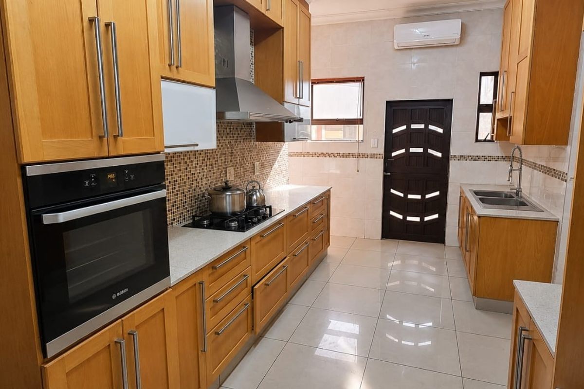 A functional kitchen featuring warm-toned wooden cabinetry, stone countertops, built-in oven, gas hob, and tiled flooring with a wall-mounted air conditioning unit.