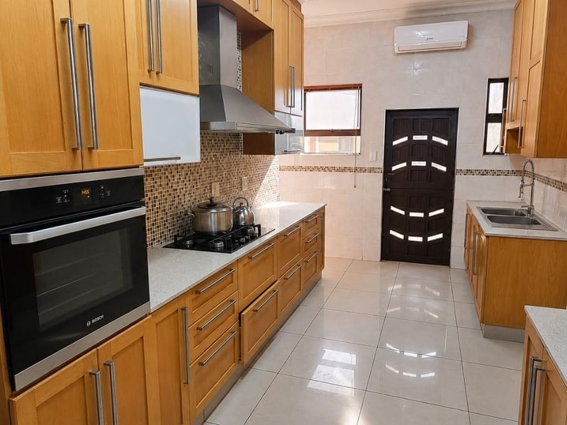 A functional kitchen featuring warm-toned wooden cabinetry, stone countertops, built-in oven, gas hob, and tiled flooring with a wall-mounted air conditioning unit.