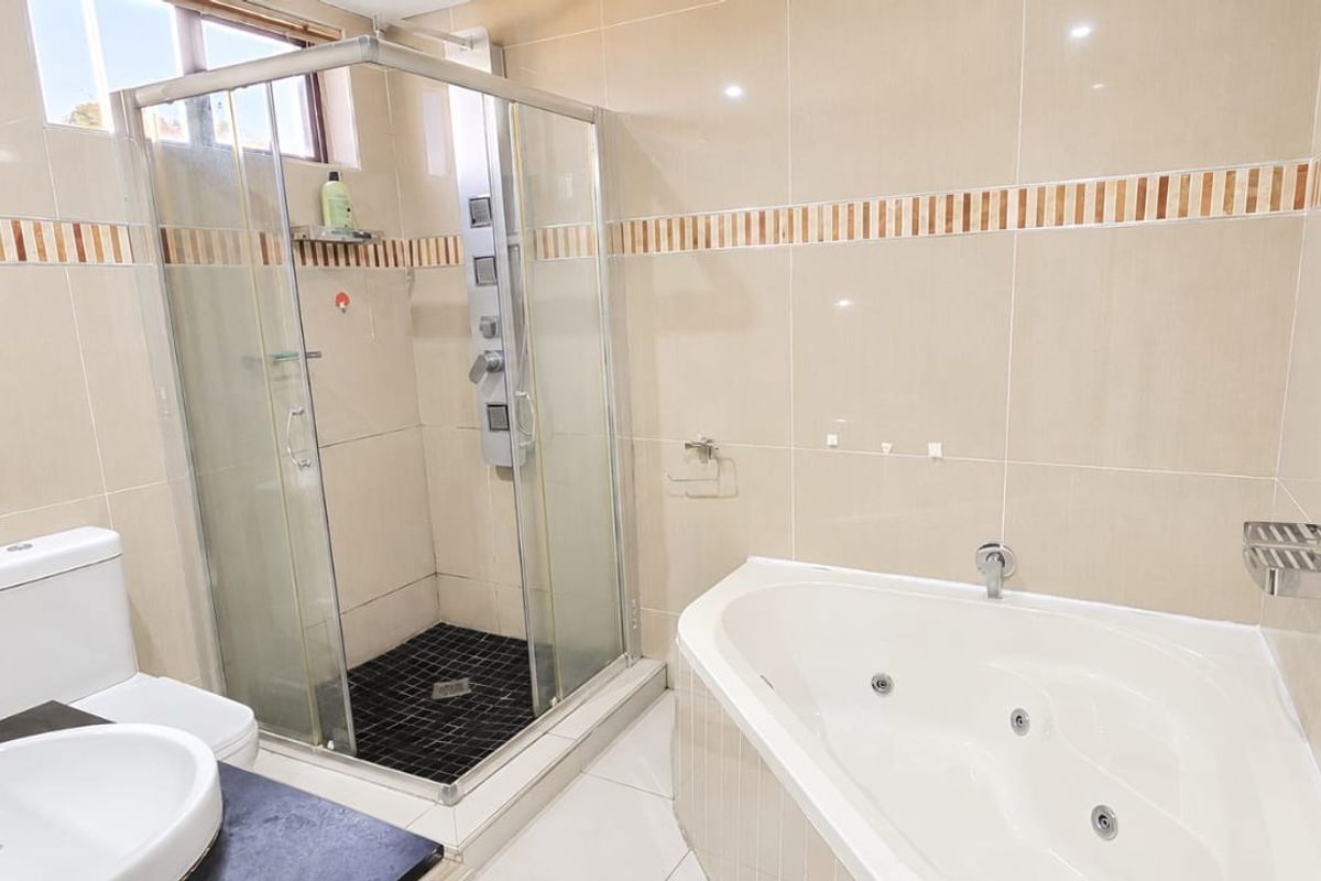 A well-appointed bathroom featuring a corner spa bath, a separate glass-enclosed shower, a vanity basin, and neutral wall tiling.
