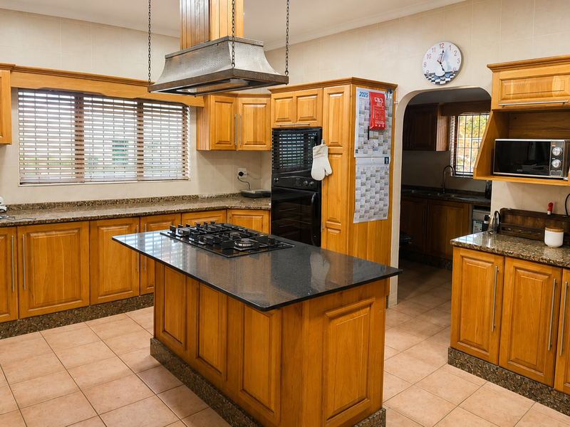 Spacious kitchen featuring extensive wooden cabinetry, granite countertops, a central island with a gas hob, and a built-in oven with an overhead extractor fan.