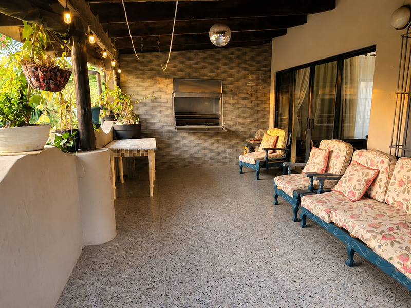 Covered patio area featuring a built-in braai, exposed timber ceiling beams, and terrazzo flooring, providing a functional outdoor entertainment space.