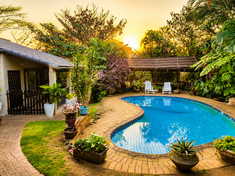 A beautifully landscaped backyard featuring a kidney-shaped swimming pool, brick-paved surround, and a covered patio area set within a lush garden.