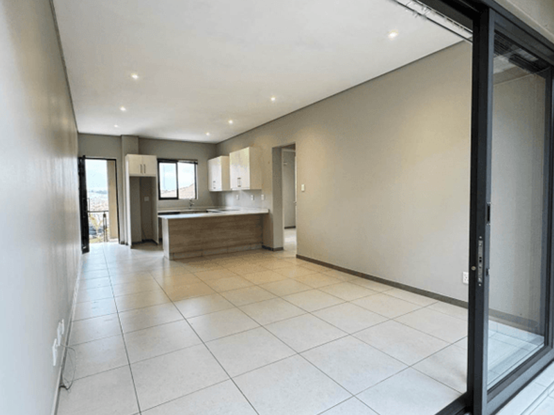 Spacious open-plan living and kitchen area featuring neutral tiled flooring, modern cabinetry, and large sliding glass doors leading to an outdoor space.
