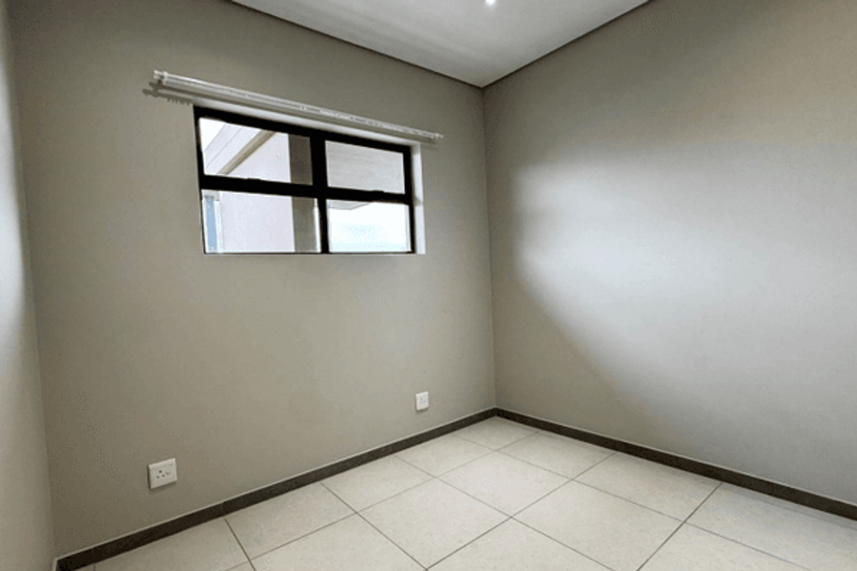 A clean, empty bedroom featuring neutral wall tones, large floor tiles, and an aluminium-framed window, providing a versatile space ready for personalization.