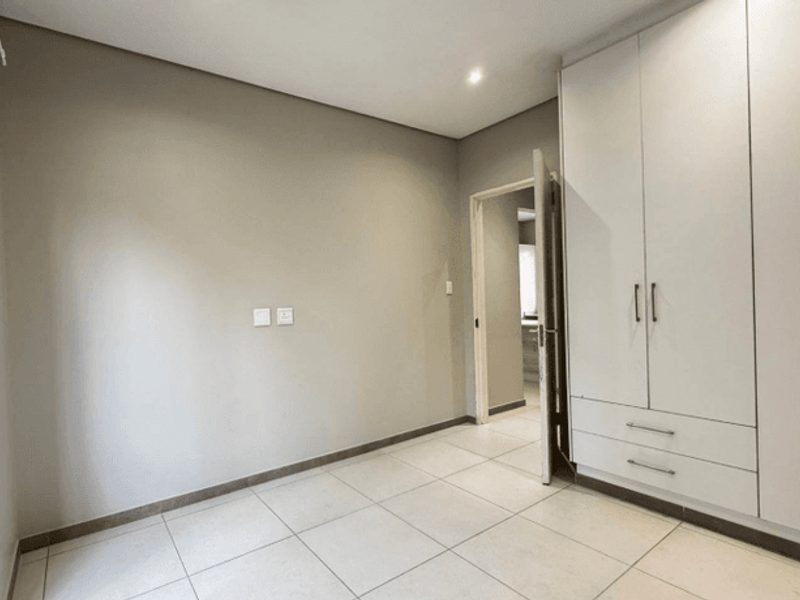 A clean, empty bedroom featuring neutral tiled flooring, recessed lighting, and ample built-in cupboard storage space.
