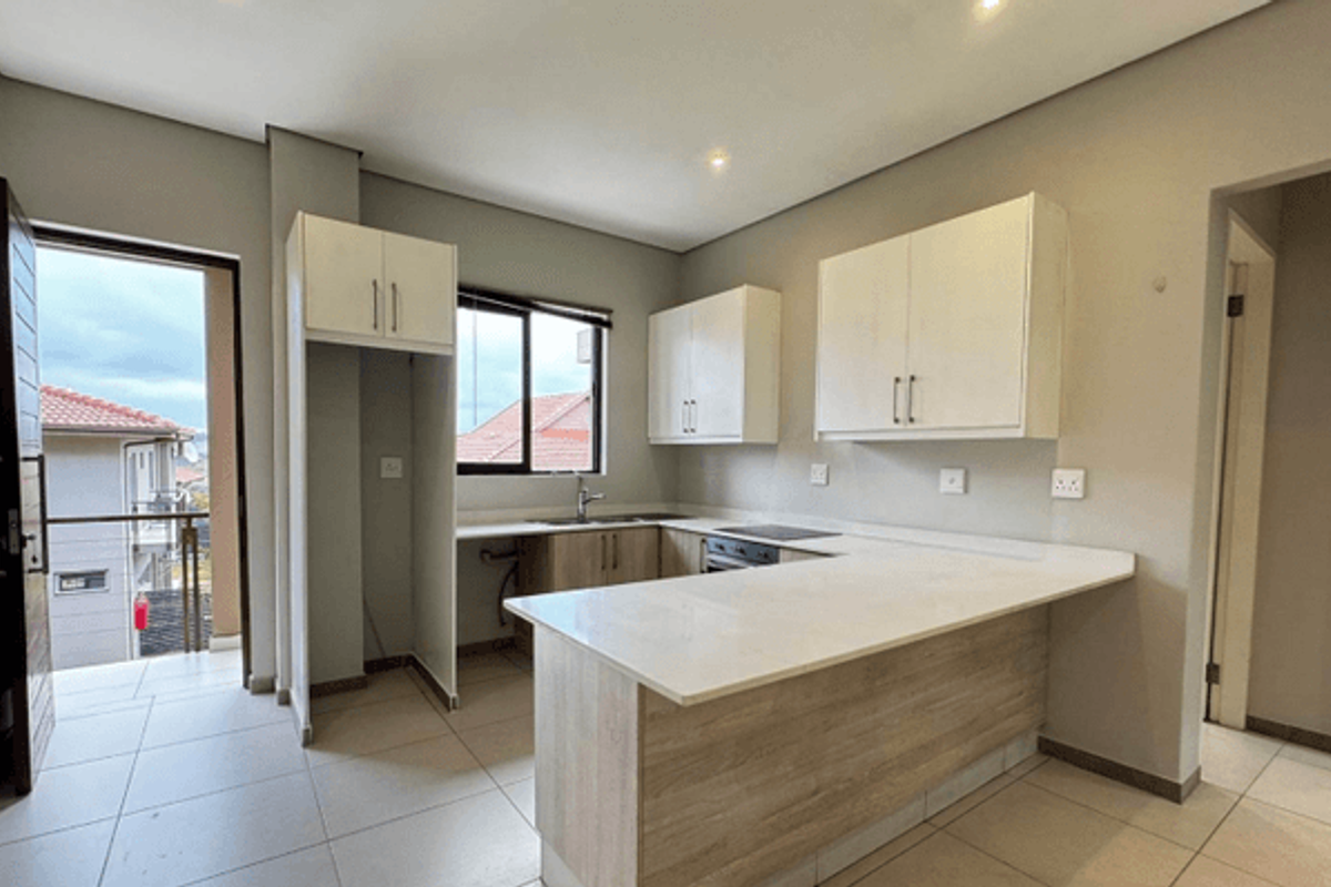 Modern kitchen featuring light wood-tone cabinetry, white stone countertops, integrated electric hob and oven, and tiled flooring with direct access to a balcony.