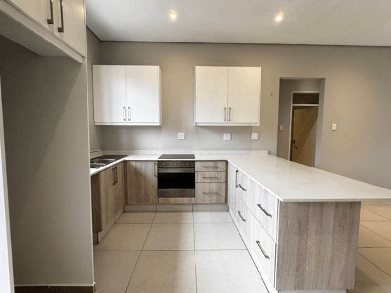 Modern kitchen featuring light wood cabinetry, stone countertops, integrated electric hob and oven, and neutral tiled flooring in an open-plan layout.