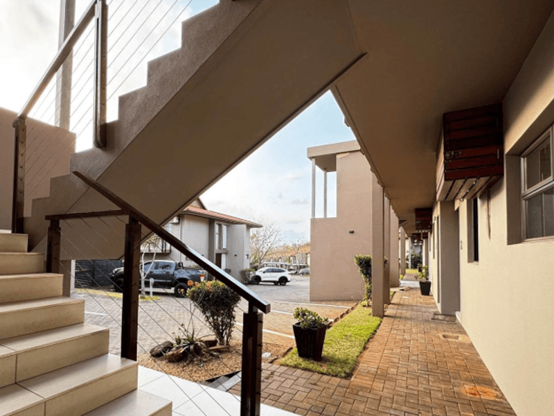 Exterior view of an apartment complex featuring a modern staircase with cable railings and a paved walkway leading to the units.