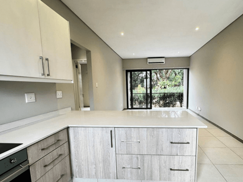 Modern open-plan kitchen and living area featuring sleek cabinetry, stone countertops, built-in oven, and sliding doors leading to an outdoor space.
