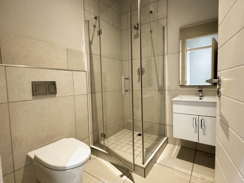 Modern bathroom featuring a wall-hung toilet, glass shower enclosure, and a sleek vanity cabinet with basin.