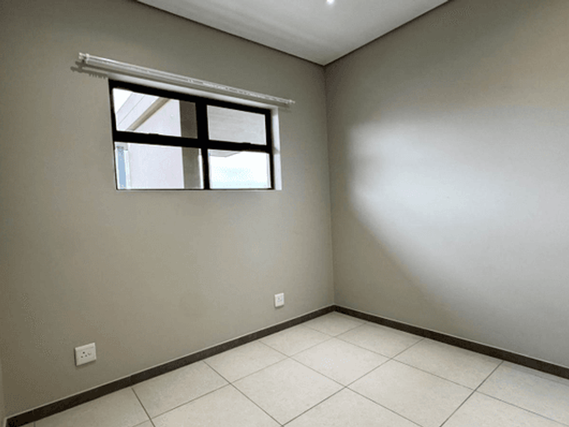 A clean, empty bedroom featuring neutral wall tones, large floor tiles, and an aluminium-framed window, providing a versatile space ready for personalization.