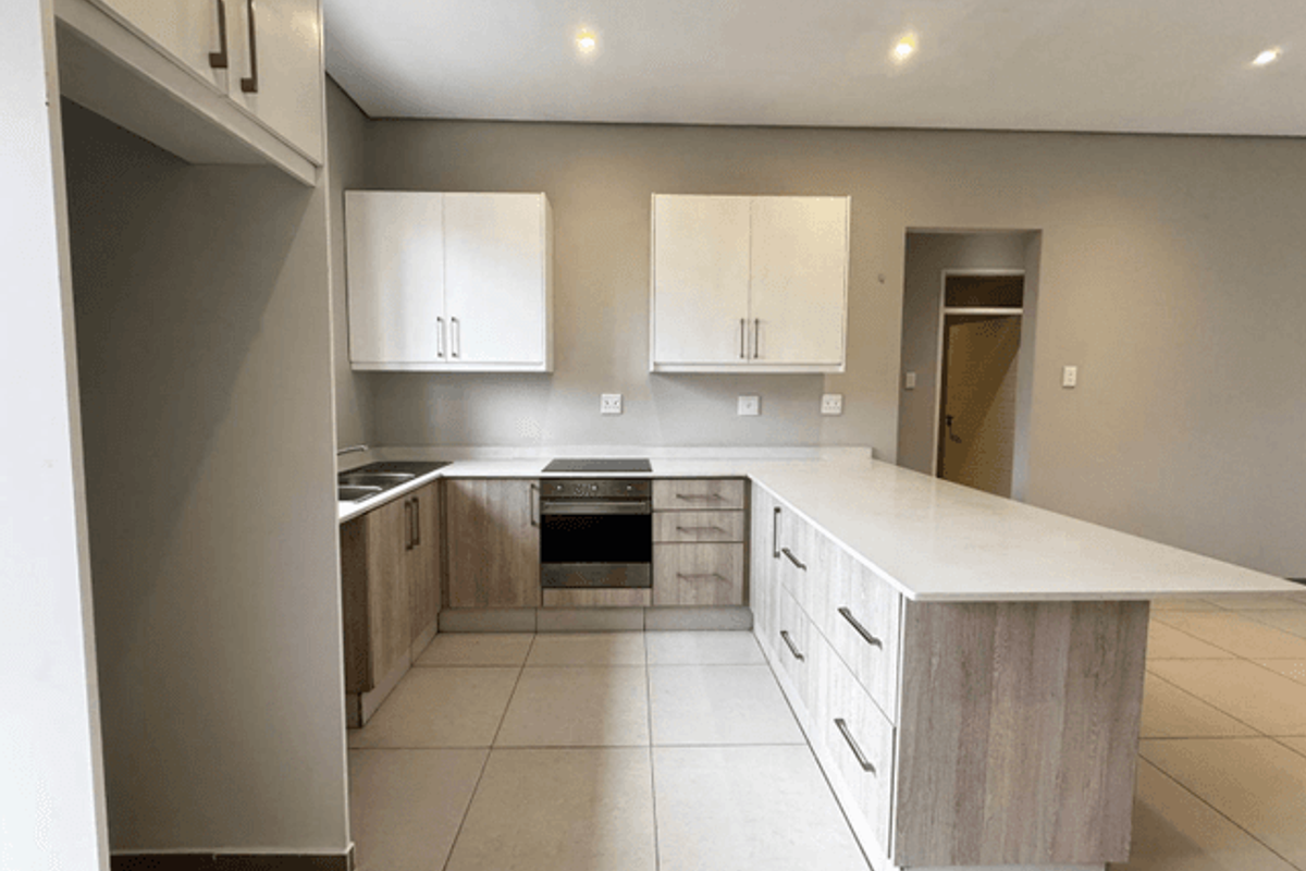 Modern kitchen featuring light wood cabinetry, stone countertops, integrated electric hob and oven, and neutral tiled flooring in an open-plan layout.