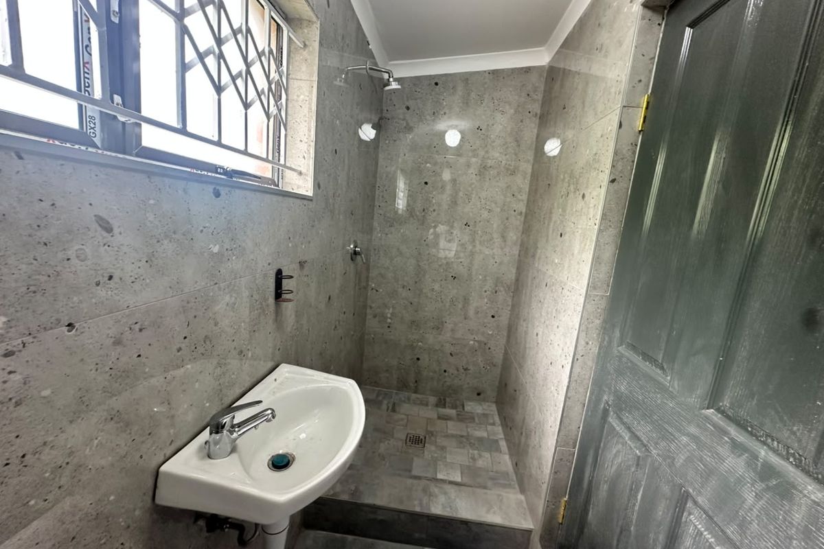 A compact bathroom featuring grey stone-look wall and floor tiles, a wall-mounted basin, and a walk-in shower area.