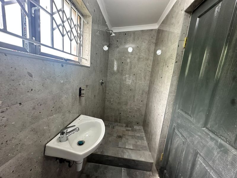 A compact bathroom featuring grey stone-look wall and floor tiles, a wall-mounted basin, and a walk-in shower area.