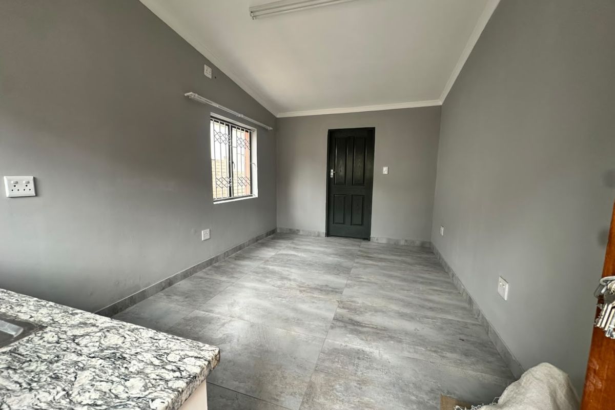 An empty open-plan living area featuring modern grey tiled flooring, neutral walls, and a granite countertop, providing a clean and versatile space.