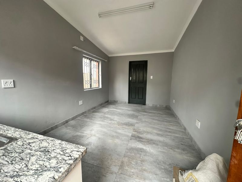 An empty open-plan living area featuring modern grey tiled flooring, neutral walls, and a granite countertop, providing a clean and versatile space.