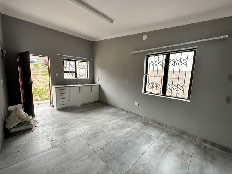 A clean, empty kitchen area featuring tiled floors, built-in cabinetry with a sink, and direct access to the exterior.