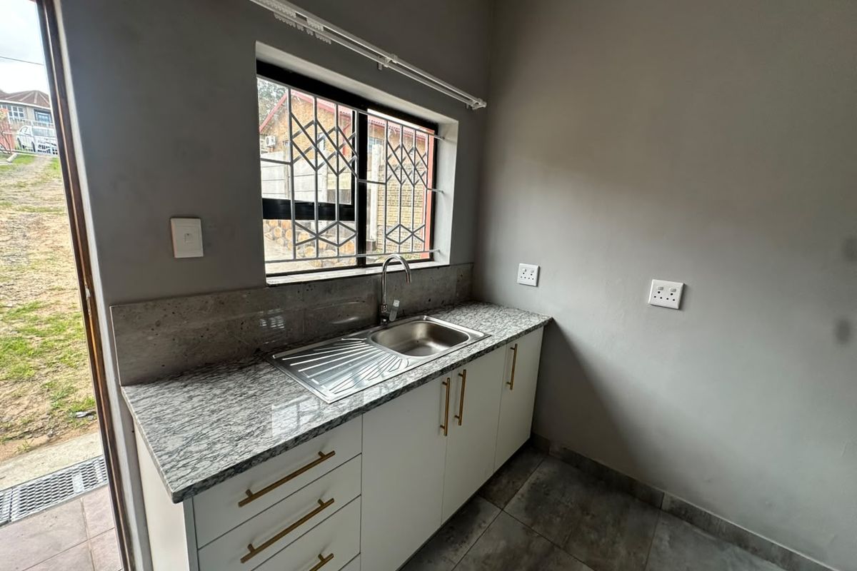 A clean, modern kitchen area featuring granite countertops, stainless steel sink, and white cabinetry with gold-tone hardware, adjacent to an exterior door.