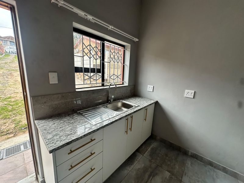A clean, modern kitchen area featuring granite countertops, stainless steel sink, and white cabinetry with gold-tone hardware, adjacent to an exterior door.