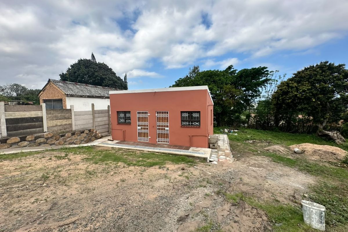 Rear view of a detached structure featuring a terracotta-colored facade, security gates, and burglar bars, set on an undeveloped plot with boundary walling.