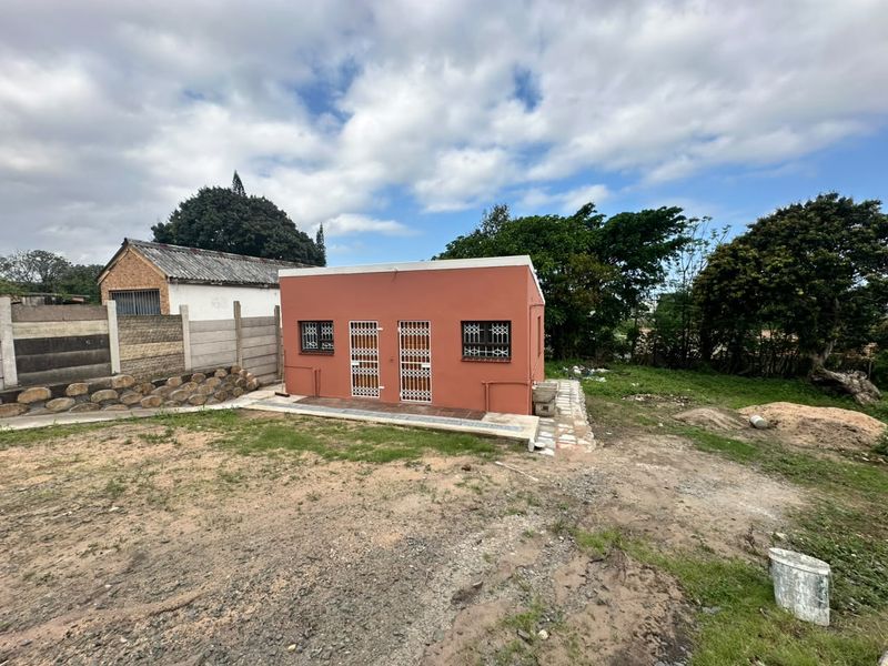 Rear view of a detached structure featuring a terracotta-colored facade, security gates, and burglar bars, set on an undeveloped plot with boundary walling.